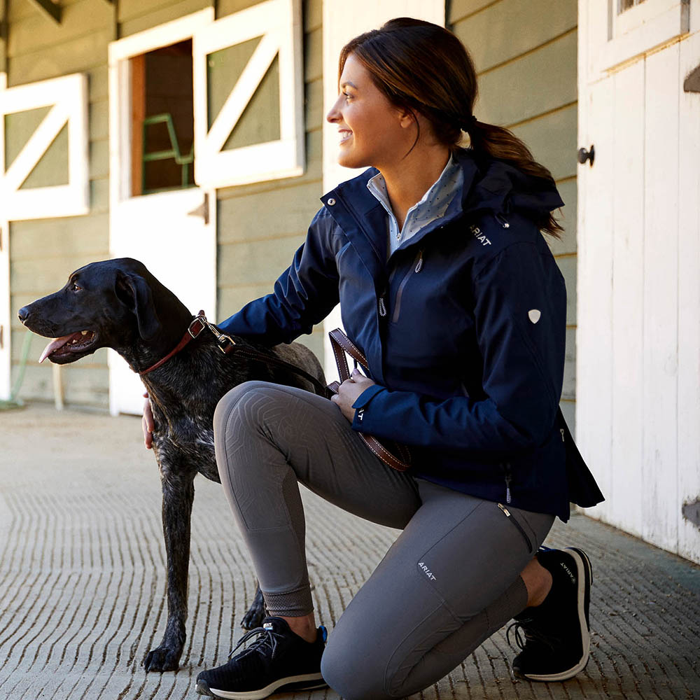 Woman with her fog on a yard wearing the Ariat Coastal Waterproof Jacket in Navy