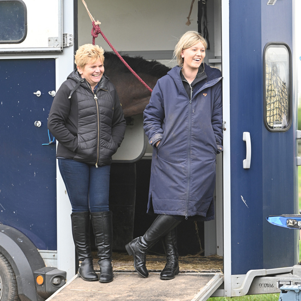 Two women stood on horse trailer wearing waterproof horse riding coats