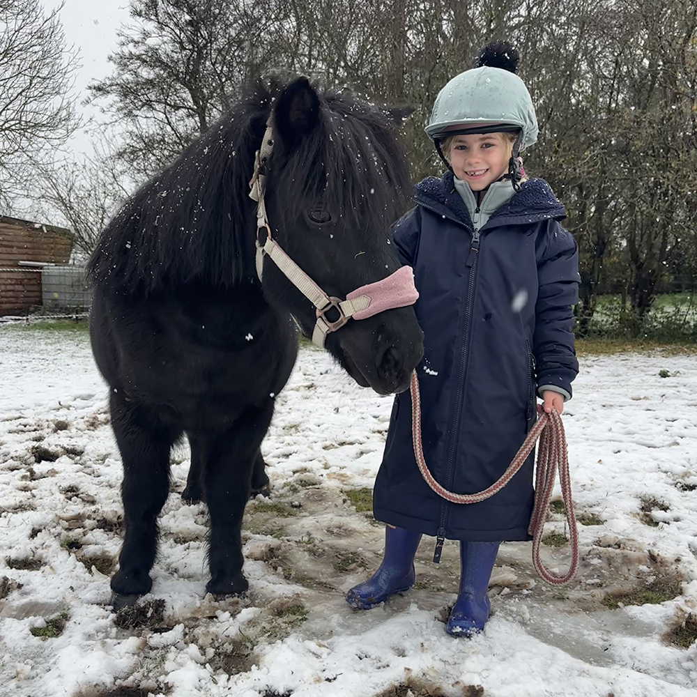 Child holding a pony wearing kids long waterproof horse rising jacket