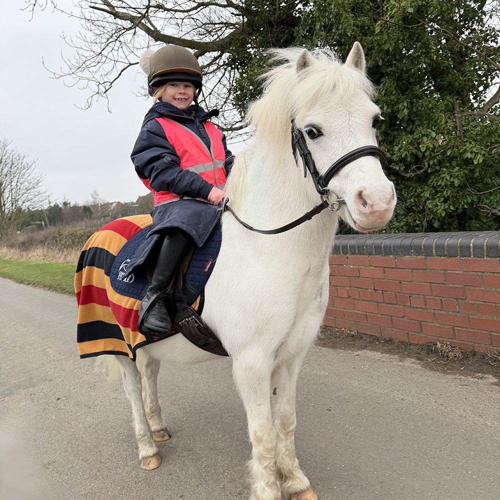 Girl wearing the Aubrion All Weather Robe riding a white pony 