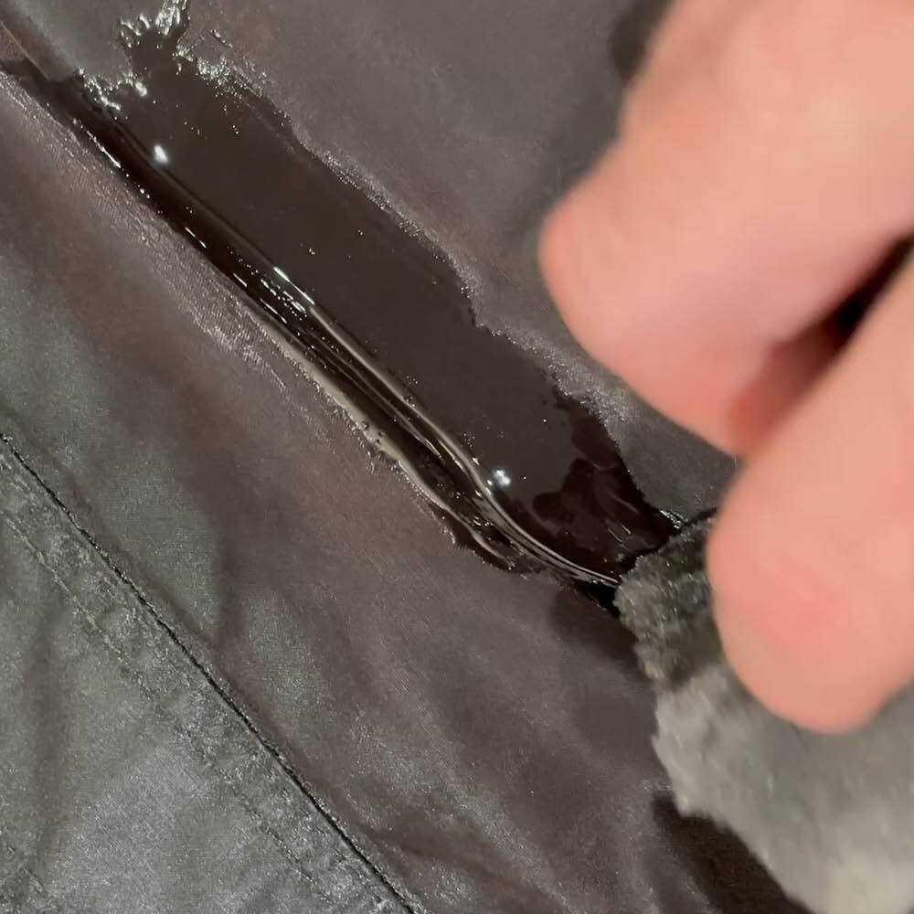 Applying melted wax dressing to the cotton fabric of a Barbour jacket during rewaxing.