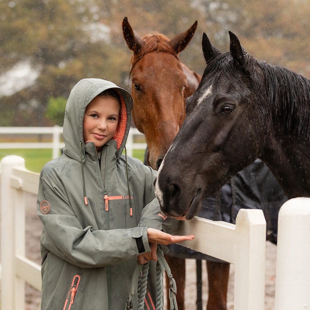 Girl wearing LeMieux Hydroshield Waterproof Riding Coat in rain with two horses