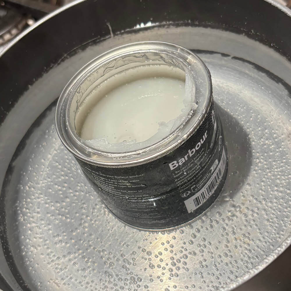 Tin of Barbour Wax Thornproof Dressing warming in a pan of hot water before application.