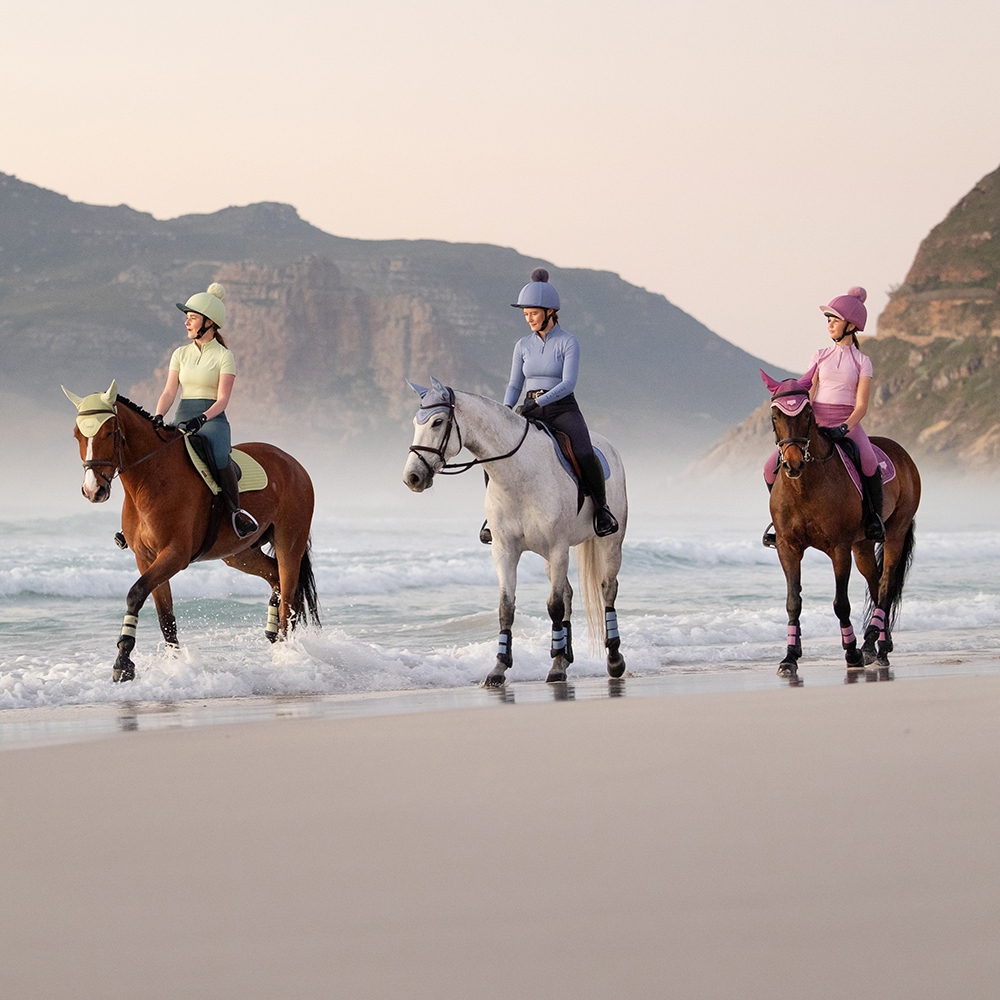 The New LeMieux Spring Summer Colours 2026 Jungle, Mallow, Powder Blue, Macaron & Fondant Three horses and their riders on a beach wearing the New LeMieux Spring Summer Colours 2026 Jungle, Mallow, Powder Blue, Macaron & Fondant