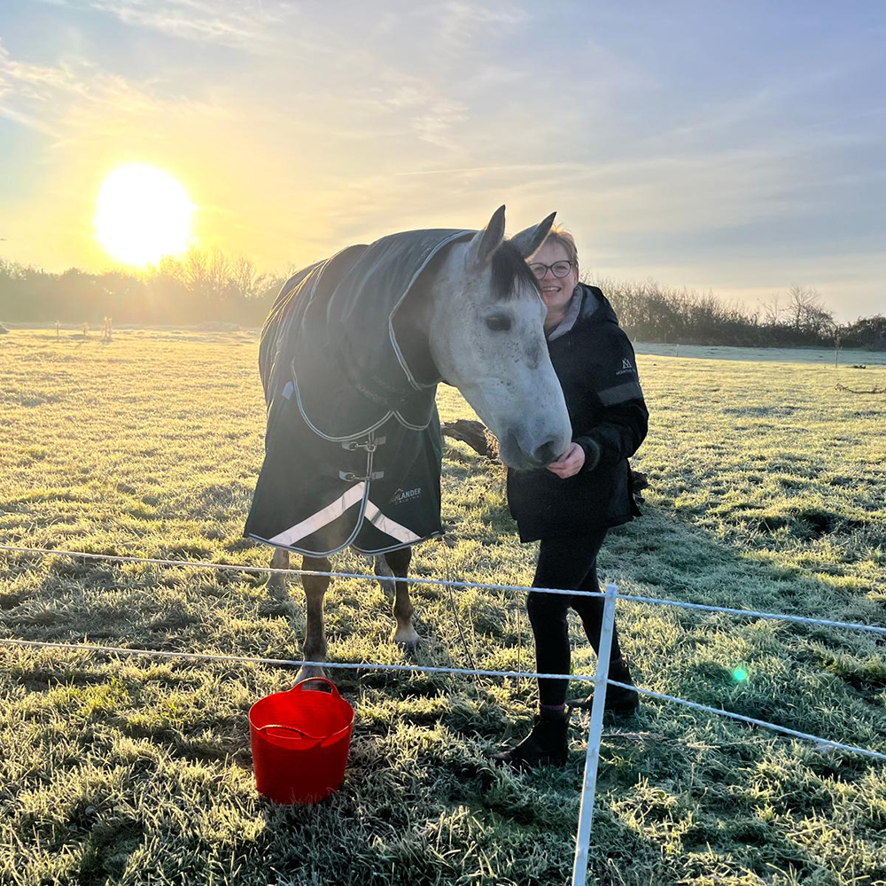 Woman stroking a grey horse that is wearing a heavyweight winter turnout rug