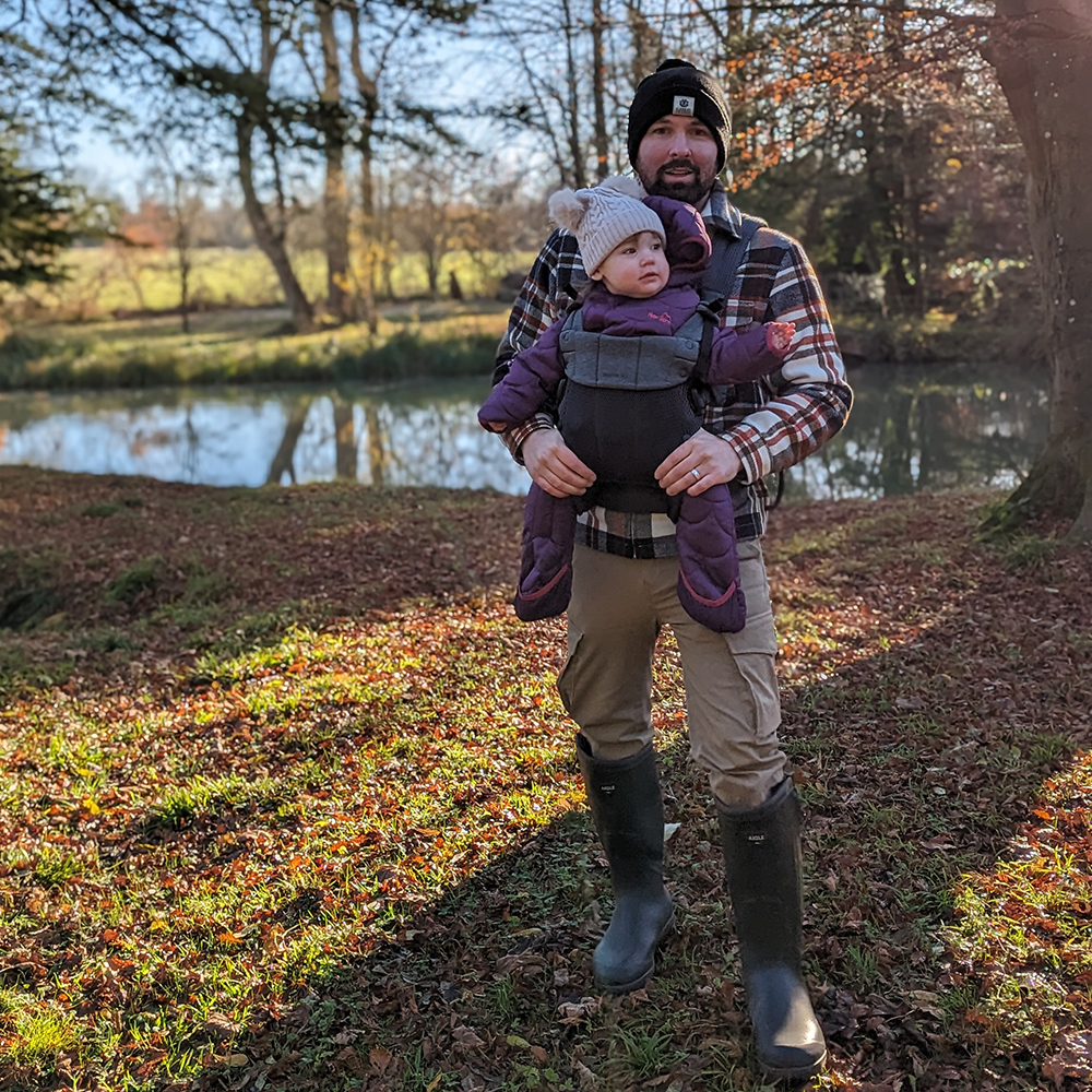 Man wearing Aigle wellies holding child in front of pond in autumn