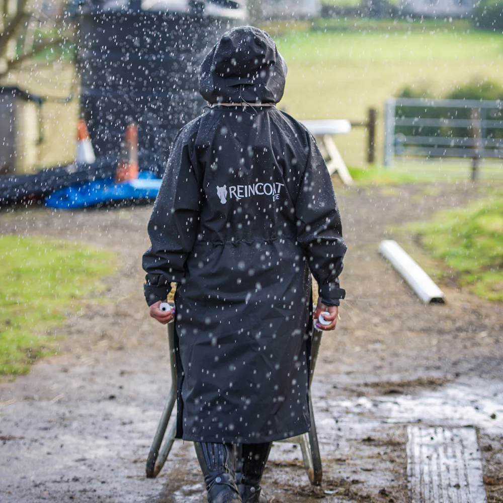 woman wearing Reincoat Pro waterproof riding coat pushing a wheelbarrow in the rain 