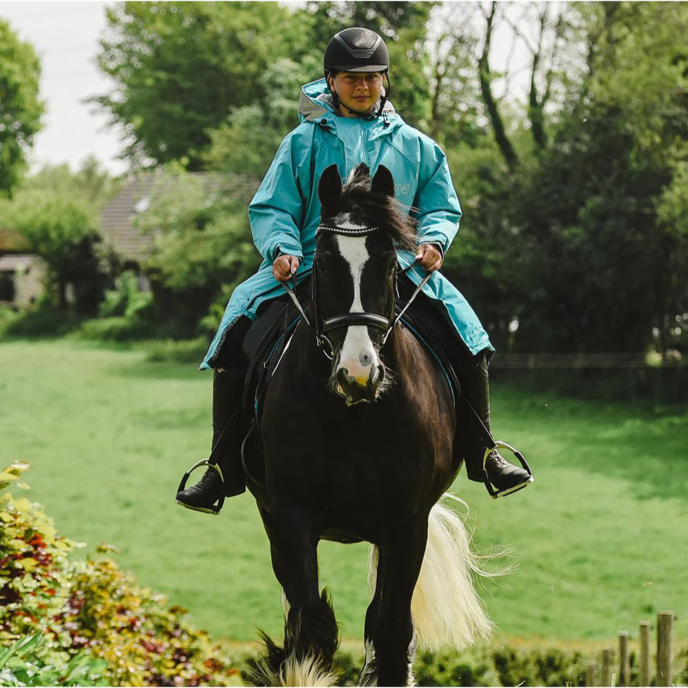 Female riding on horse wearing the Reincoat Waterproof Horse Riding Jacket in Blue