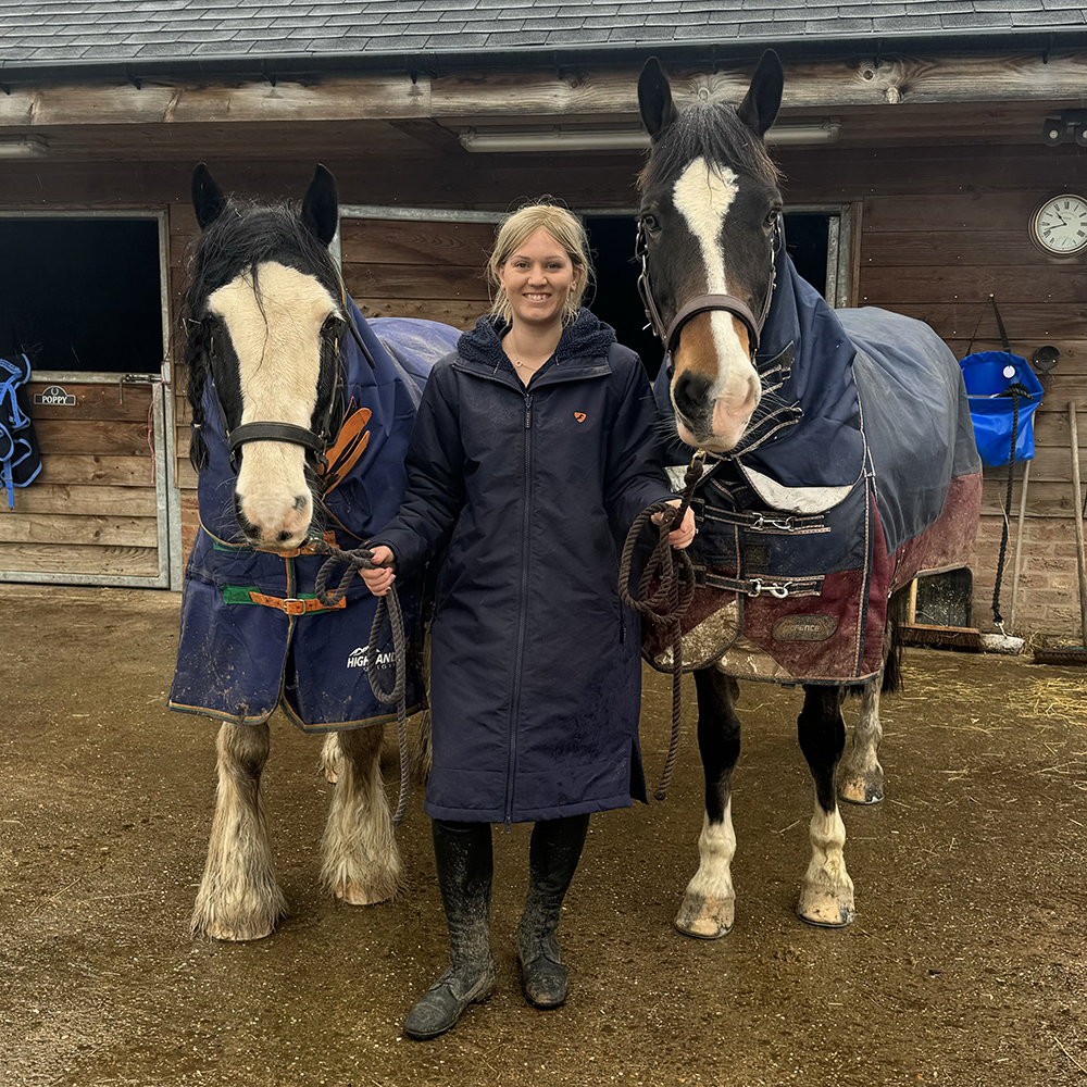 Woman holding two horses wearing long waterproof horse riding coat