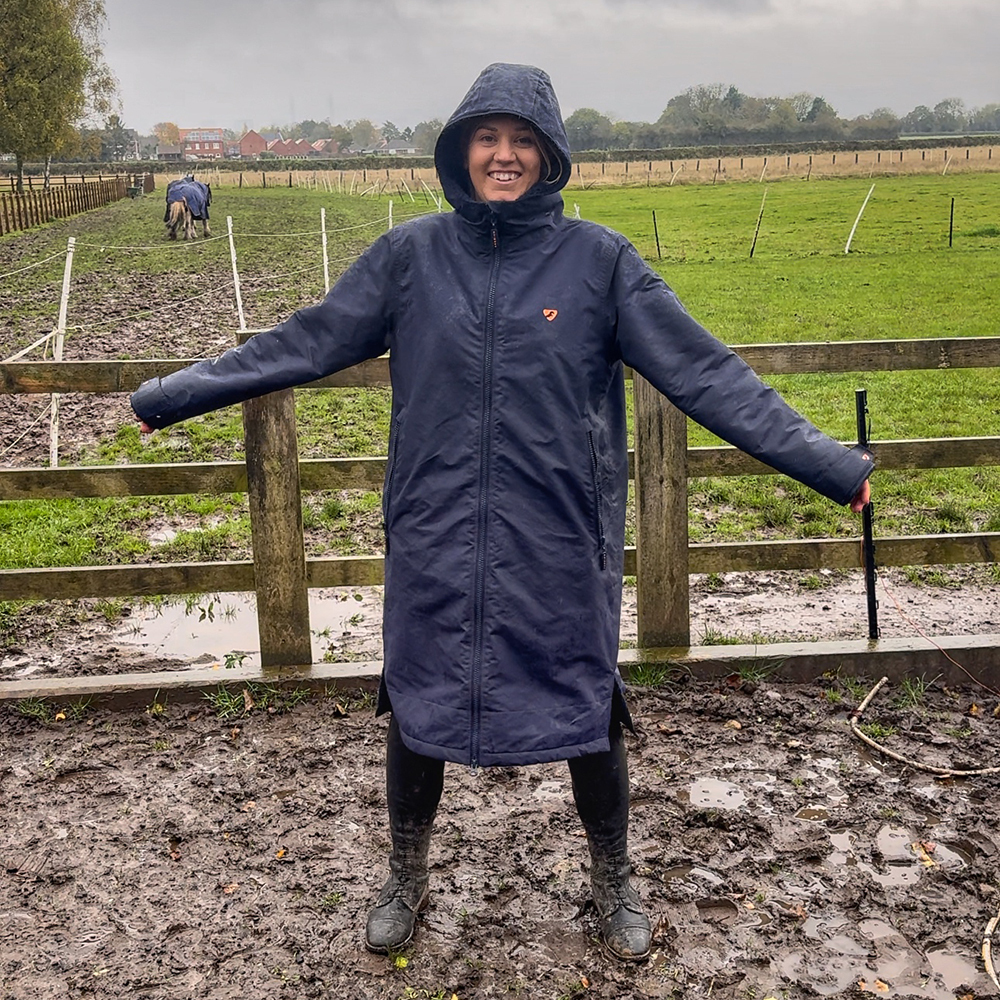 Woman wearing the ladies Woman riding horse wearing Aubrion All Weather Robe in rain and muddy field 