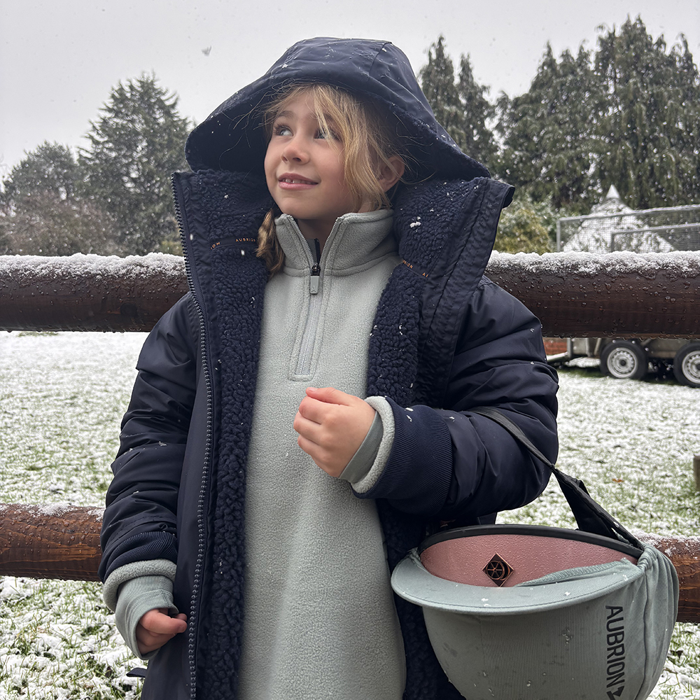 Young equestrian wearing a waterproof horse riding coat with hood 