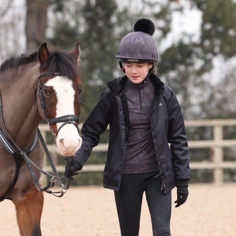 Young rider dressed in waterproof horse riding clothing during winter lesson